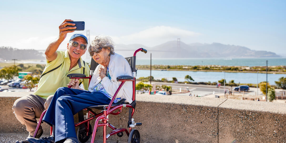 Elderly couple poses for a selfie before the Golden Gate Bridge at Presidio Tunnel Tops.