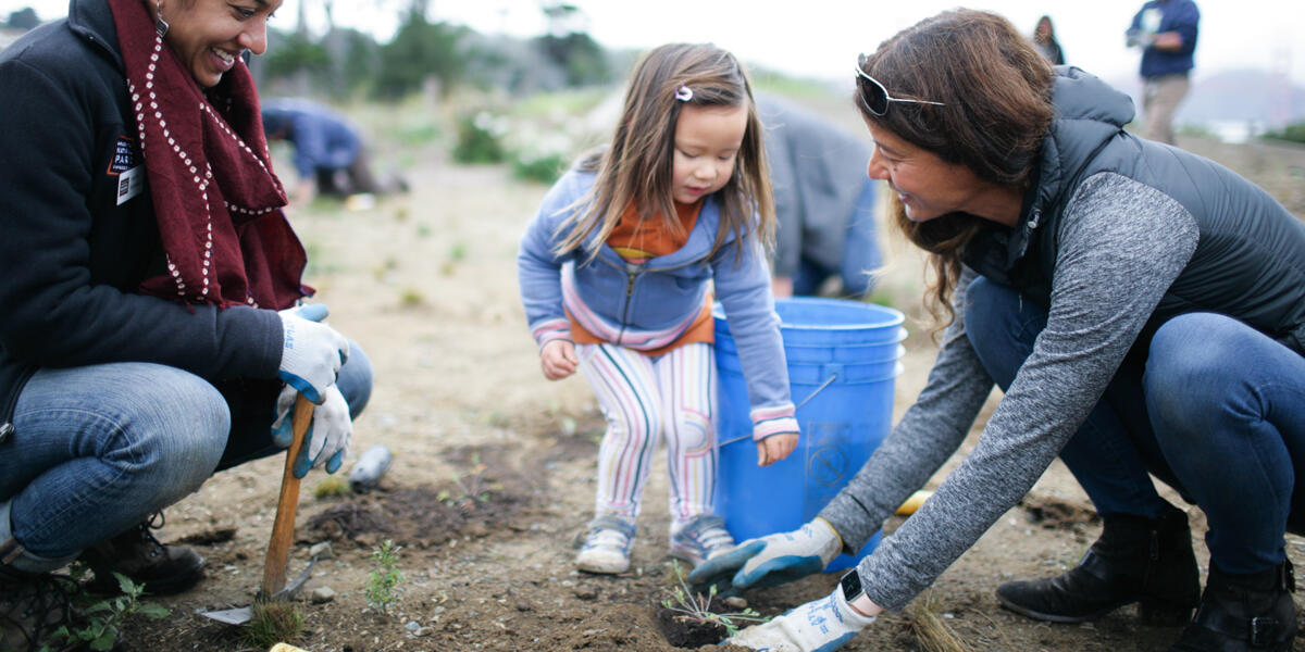 Parks Conservancy staff and volunteers smiling as they plant saplings in the parks.