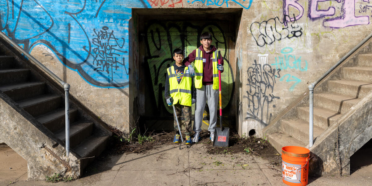 Two youthful volunteers in bright vests standing before the concrete wall at the Presidio Golden Gate Overlook battery