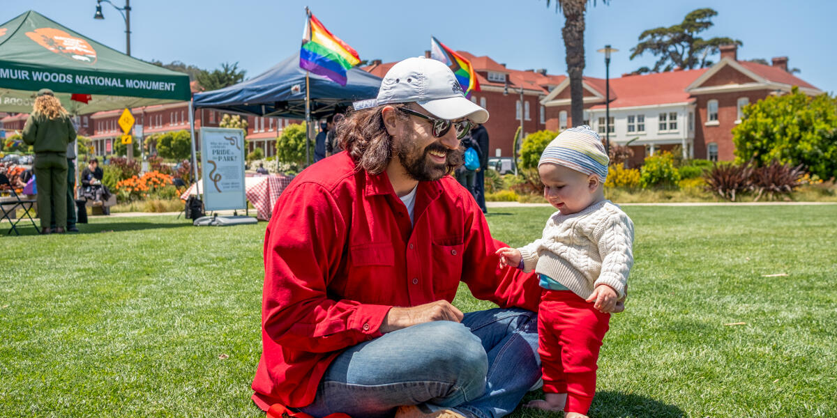 A father and child sit on the Presidio lawn during Pride at the Presidio event.