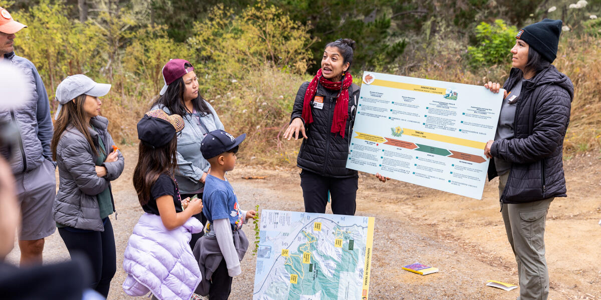 Parks Conservancy Community Engagement staff holding a sign, informing the local community at Rancho Corral de Tierra.