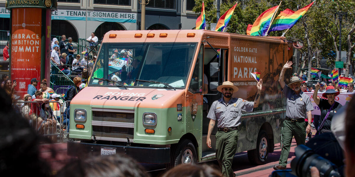 NPS park ranger marches alongside the Roving Ranger mobile trailhead at the 2022 SF Pride parade.