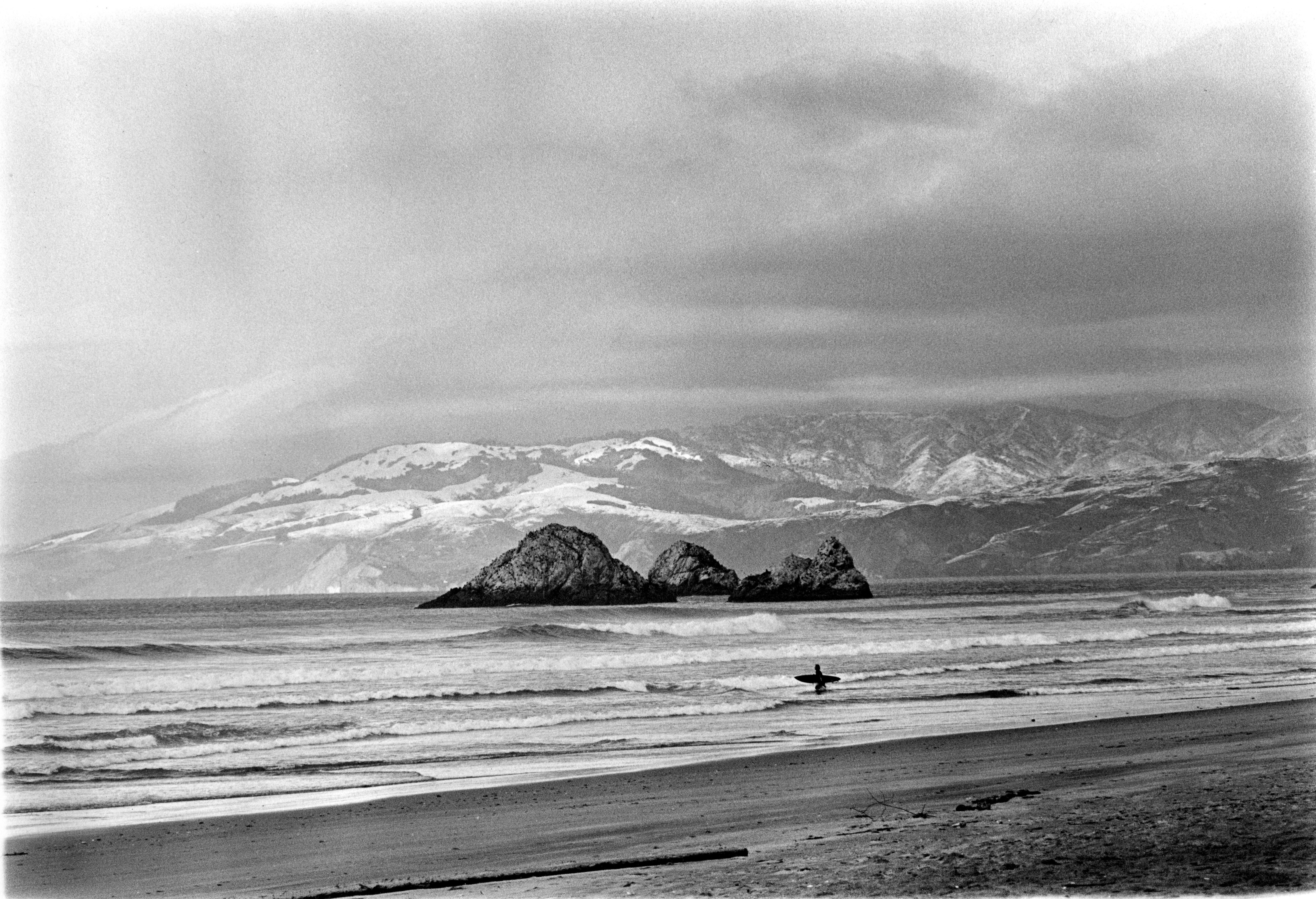 Surfer at Ocean Beach with snowy Marin Headlands in background