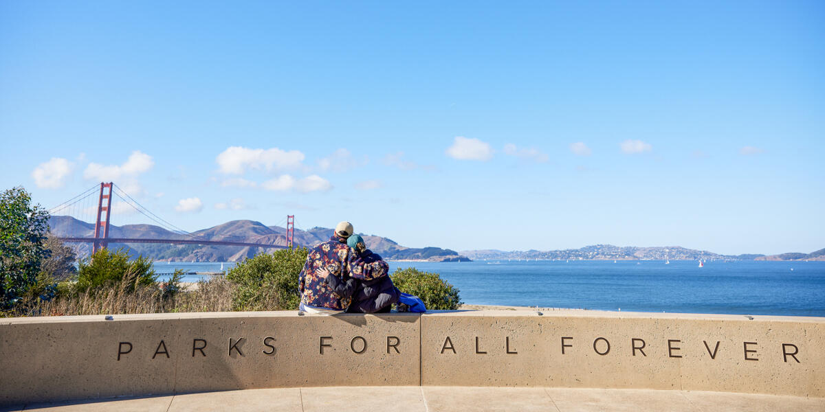 A embracing couple sits and looks out at the golden gate bridge, marin headlands, and san francisco bay