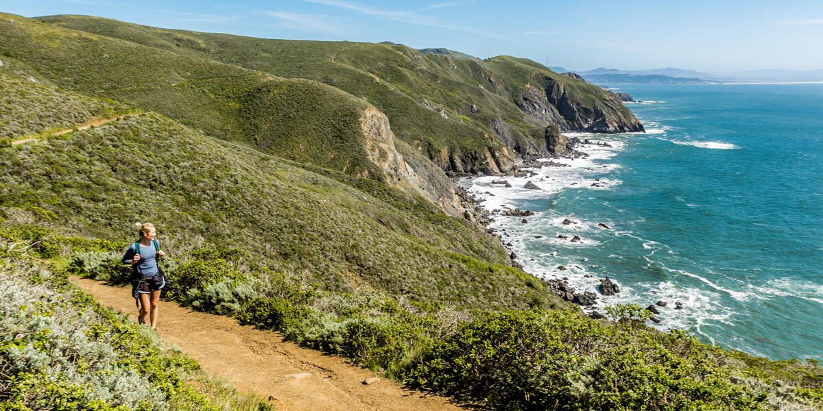 A hiker looks out at scenic view of the pacific coastline from the Coastal Trail in Marin Headlands on a bright sunny day.