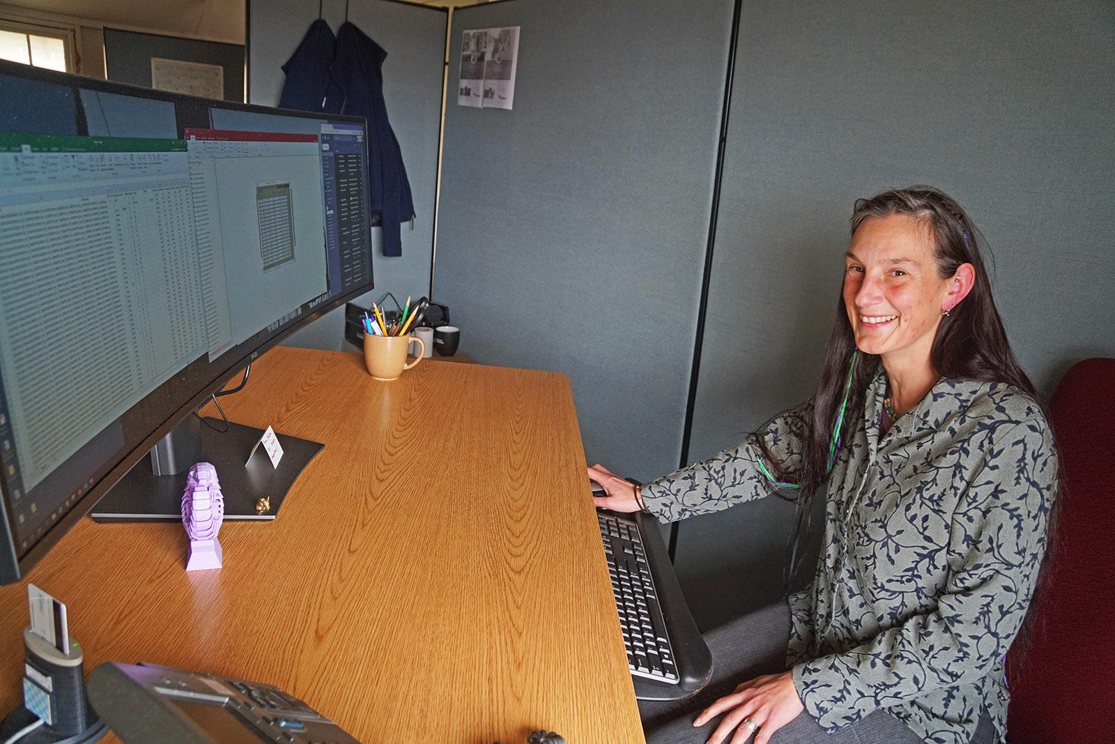 Lizzy Edson smiles behind a large curved computer monitor.