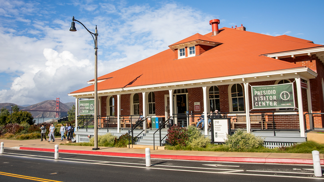 A scenic photo of the Presidio of San Francisco William Penn Mott, Jr. Visitor Center on a sunny day with the golden gate bridge seen in the background.