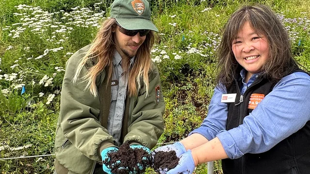 Two people hold up coffee grounds for a park project