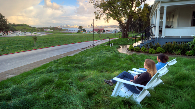 Two people sit in chairs and look out over a grassy field at the San Francisco skyline