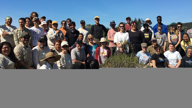 A large group of volunteers poses outside on a sunny day