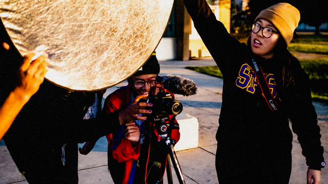 Crissy Field Center youth program participants working a photoshoot, holding a camera and light reflector.