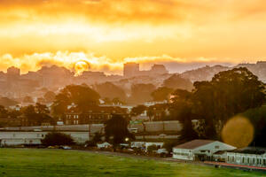 The bright yellow sun rises and shines through clouds over San Francisco skyline and Crissy Field.