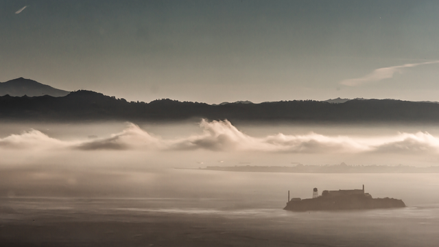 Alcatraz Island is pictured in the distance with dramatic gray clouds overhead.