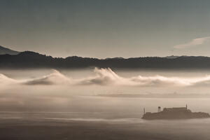 Alcatraz Island is pictured in the distance with dramatic gray clouds overhead.