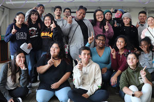 A group of smiling teenagers poses together inside of a room.