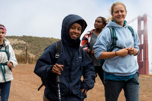 Four hikers trek down the SCA Trail in the Marin Headlands with the Golden Gate Bridge in the background.