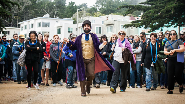 Person in costume leading a crowd of audience members through a park
