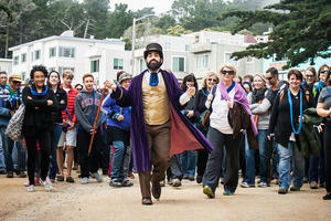 Person in costume leading a crowd of audience members through a park