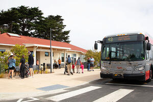 A red and gray San Francisco Muni bus parked at a station in the Presidio