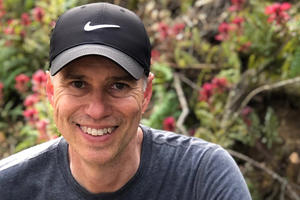 A volunteer smiles while seated in front of a blooming hedge