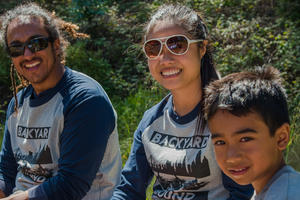 Two adults and a young boy sit together outdoors in bright sun.