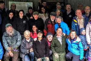 A large group smiles while posing for a photo in front of a metal barn.