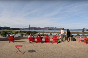 The view of the Golden Gate Bridge from Presidio Tunnel Tops. People relax in the signature red Adirondack chairs to take in the sights.