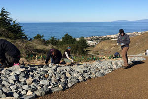 A small group of people focus on individual tasks while working outside on a trail overlook a body of water