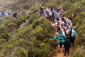 people standing on a trail waving at the camera with bushes in landscape