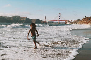 Child plays in the waves with Golden Gate Bridge in background.