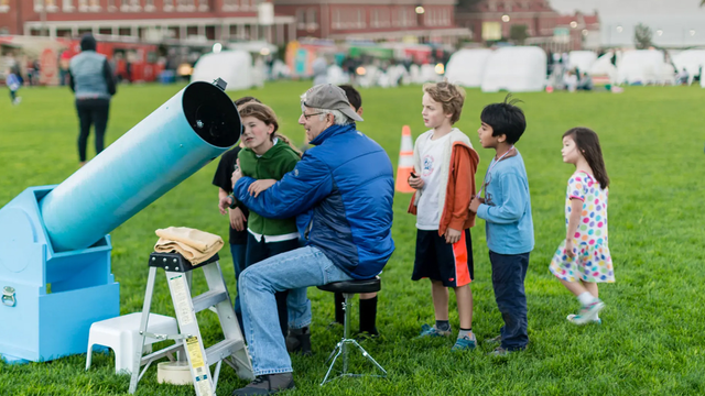 Children watching an astronomer adjust a telescope on the Presidio Main Lawn for stargazing