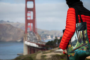 Person holds a tote bag with forest scene while gazing at the Golden Gate Bridge.