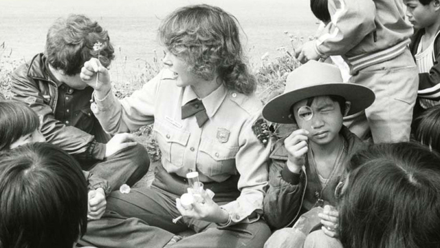 NPS park ranger, children gather and examine flowers in black and white historic photo from 1978.