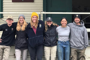 A group of interns pose together outside of a building while smiling at the camera