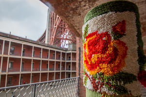 Pole covered in yarn with Fort Point and Golden Gate Bridge in background.