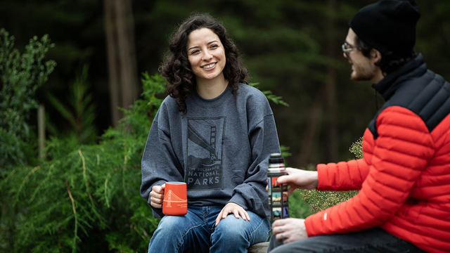 Two people talk and hold mugs with parks in the background.