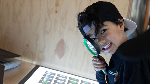 Youth with magnifying glass looking at slides at Presidio Tunnel Tops.