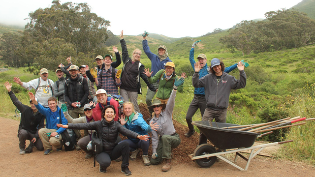 A group of volunteers joyfully pose after working outside on a trail