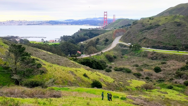 Three people stand on a hillside overlooking the Golden Gate Bridge