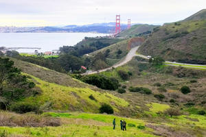 Three people stand on a hillside overlooking the Golden Gate Bridge
