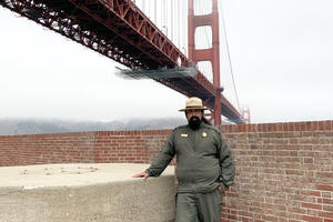 NPS Ranger Erick Cortes stands in front of the Golden Gate Bridge at Fort Point Historic Site.