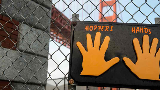 Sign labeled "Hopper's Hands" on a fence with the Golden Gate Bridge behind.