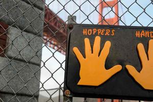 Sign labeled "Hopper's Hands" on a fence with the Golden Gate Bridge behind.