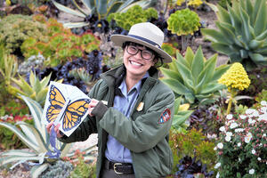 Ranger Rebecca Au poses with a butterfly drawing in a flower field.