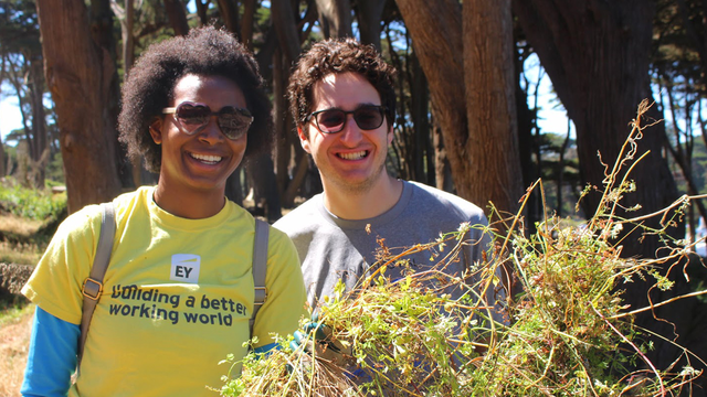two people smile for the camera while holding plants they removed during a volunteer event