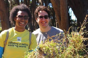 two people smile for the camera while holding plants they removed during a volunteer event