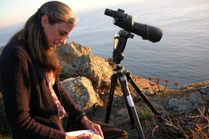 Biologist Sarah Allen records data in a notebook next to rocky California coastline.