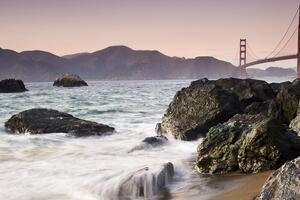 Waves crashing over rocks at Marshall's Beach with Golden Gate Bridge in the background.