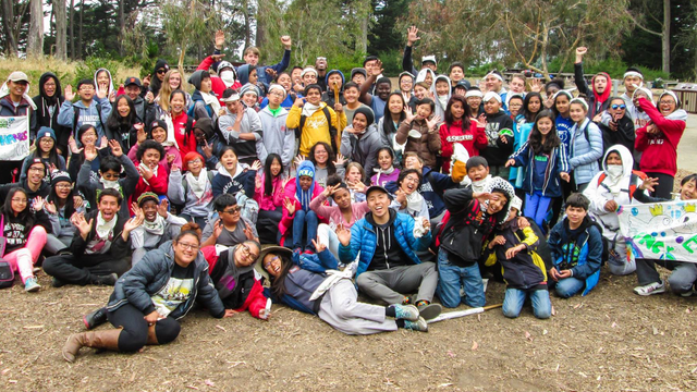 A large group of cheerful teenagers excitingly cheer at Rob Hill Campground in the Presidio of San Francisco