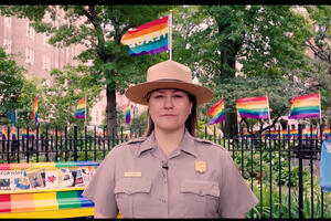National Park Service Ranger Jamie Adams stands at the Stonewall National Monument with a backdrop of rainbow flags in celebration of Pride Festival.